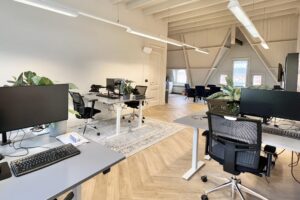 Modern ingericht kantoor op Paulus Potterstraat met bureaus, computerschermen, bureaustoelen en planten in een lichte ruimte met houten vloer.